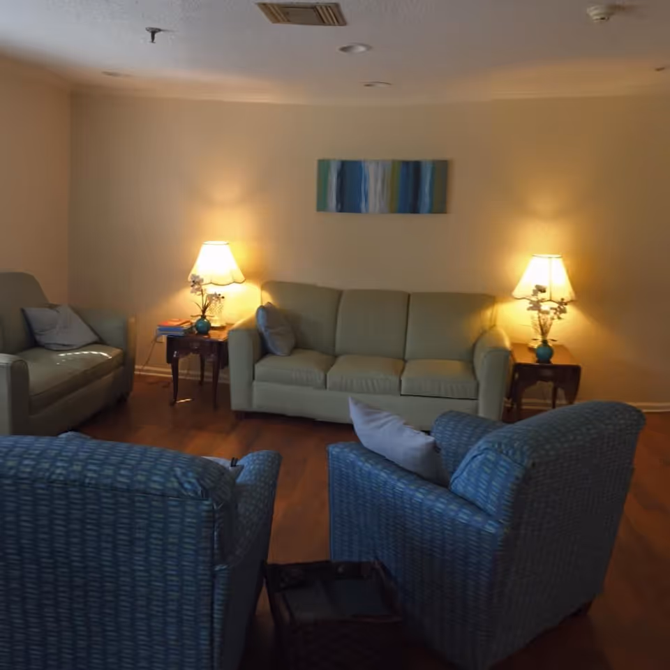 Cozy living room with a sofa and armchairs arranged around side tables with lamps and wall art.
