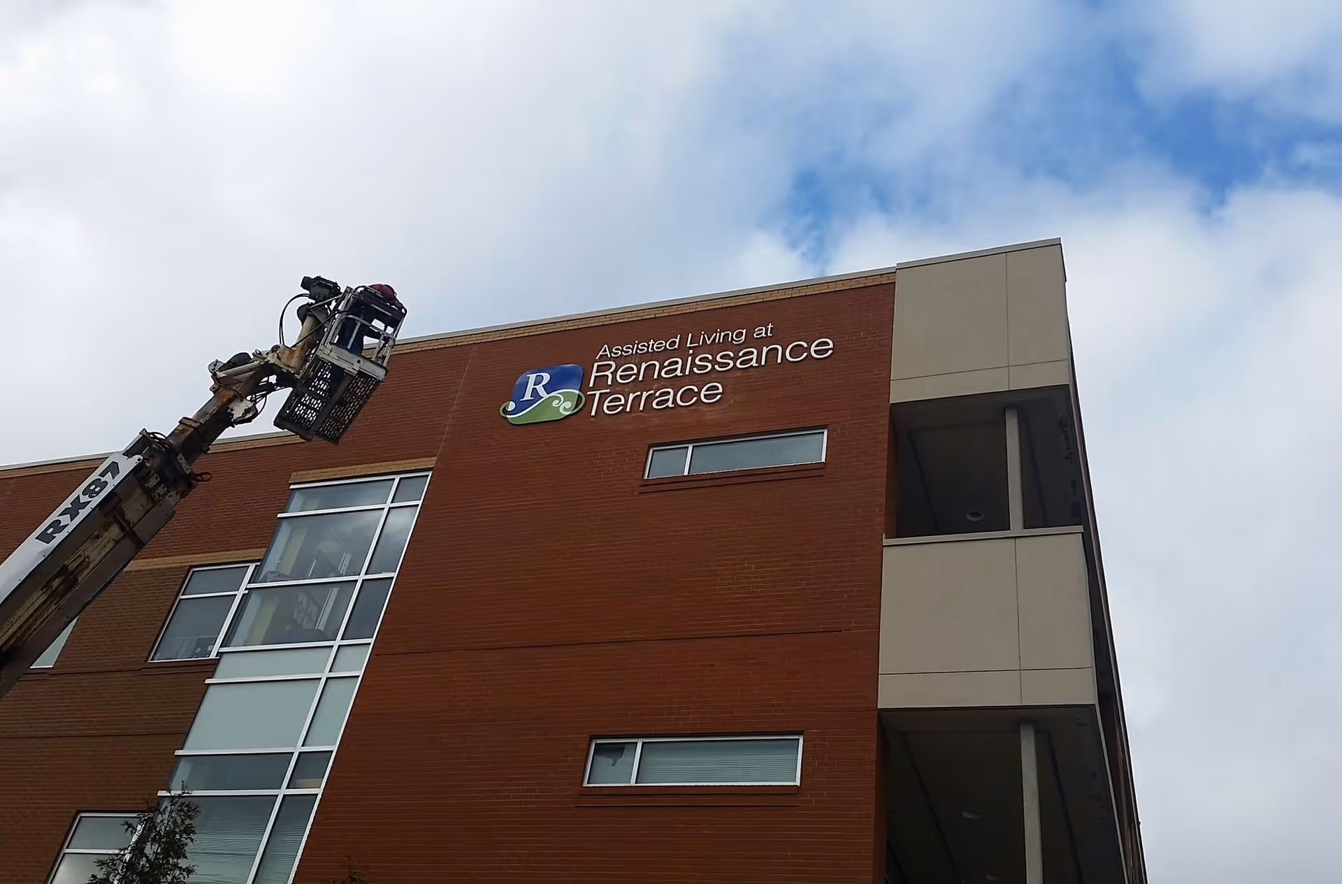 Exterior view of a multi-story assisted living facility named Renaissance Terrace with a worker in a lift basket performing maintenance or installation near the building's sign.