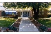 Entrance to a brick senior living facility with a walkway, landscaping, and a large tree.