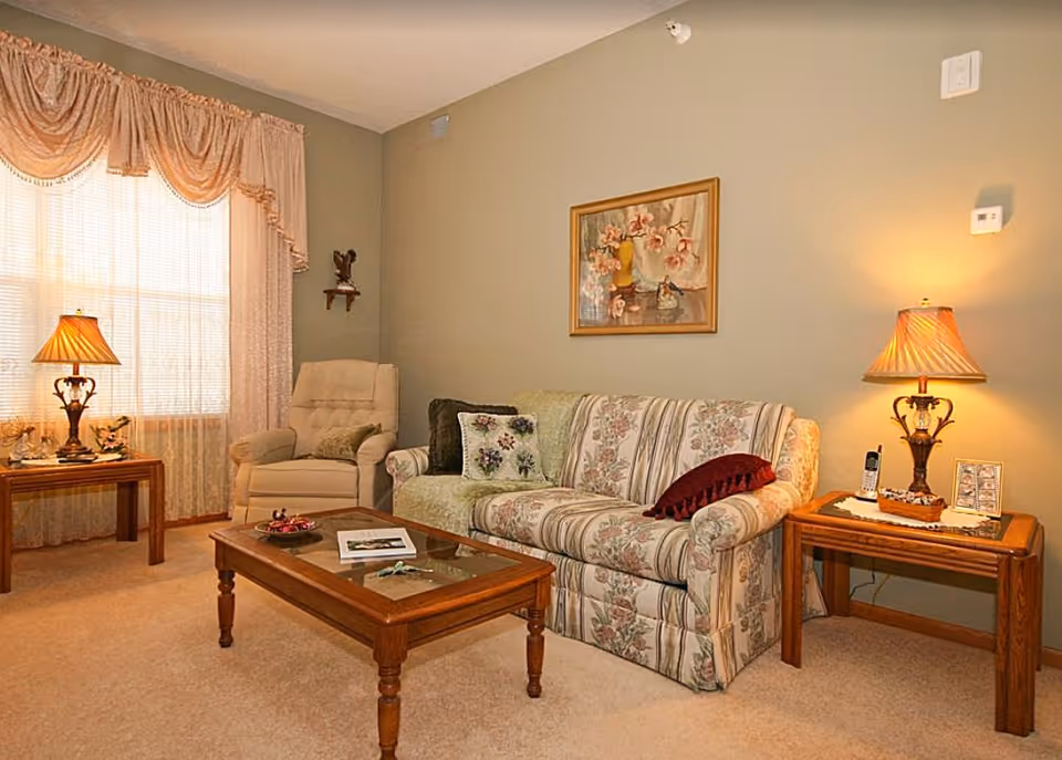 Cozy living room with a floral-upholstered sofa, armchair, wooden coffee and side tables, and lit table lamps.