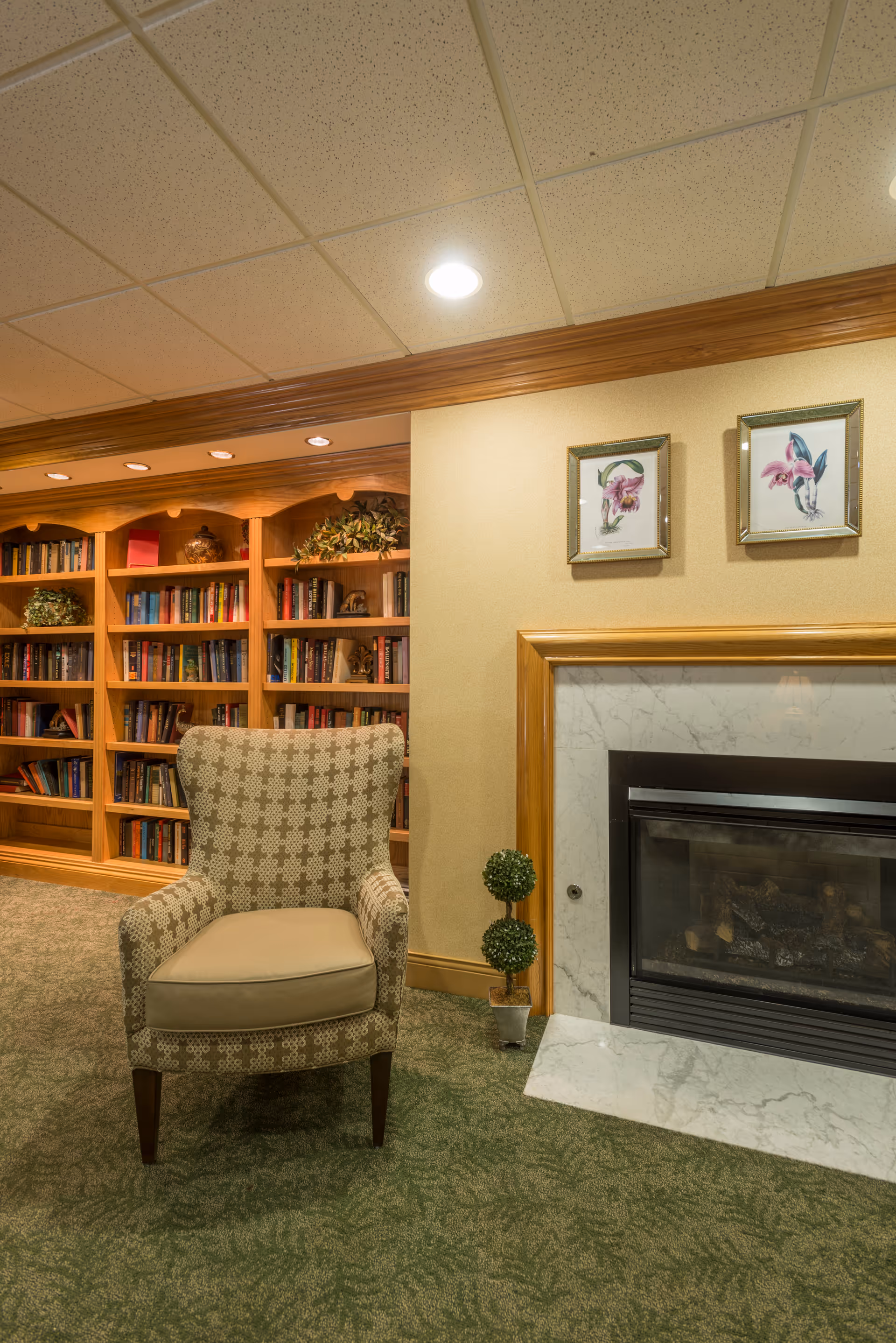 A cozy lounge area with an upholstered armchair in front of a fireplace and a built-in bookshelf.