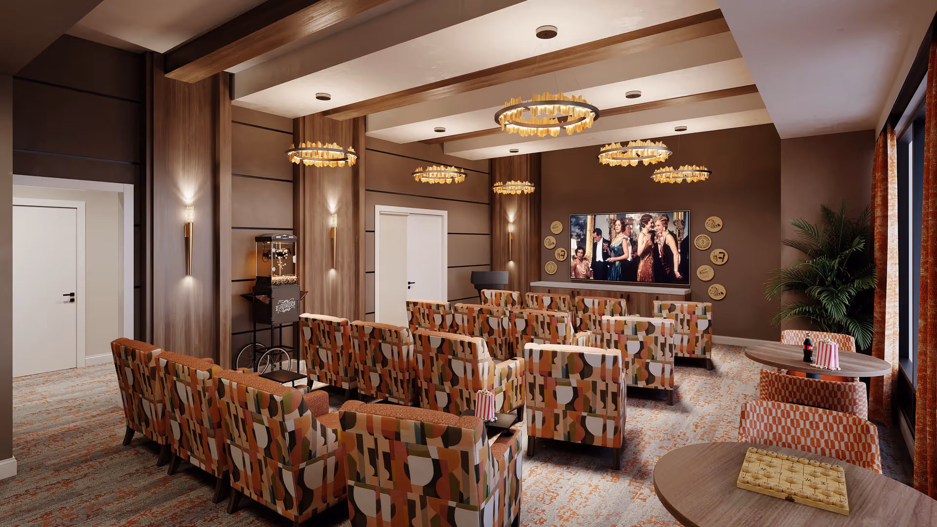 A cozy screening room with rows of patterned armchairs facing a large wall-mounted TV, chandeliers, a popcorn cart, and small round tables.