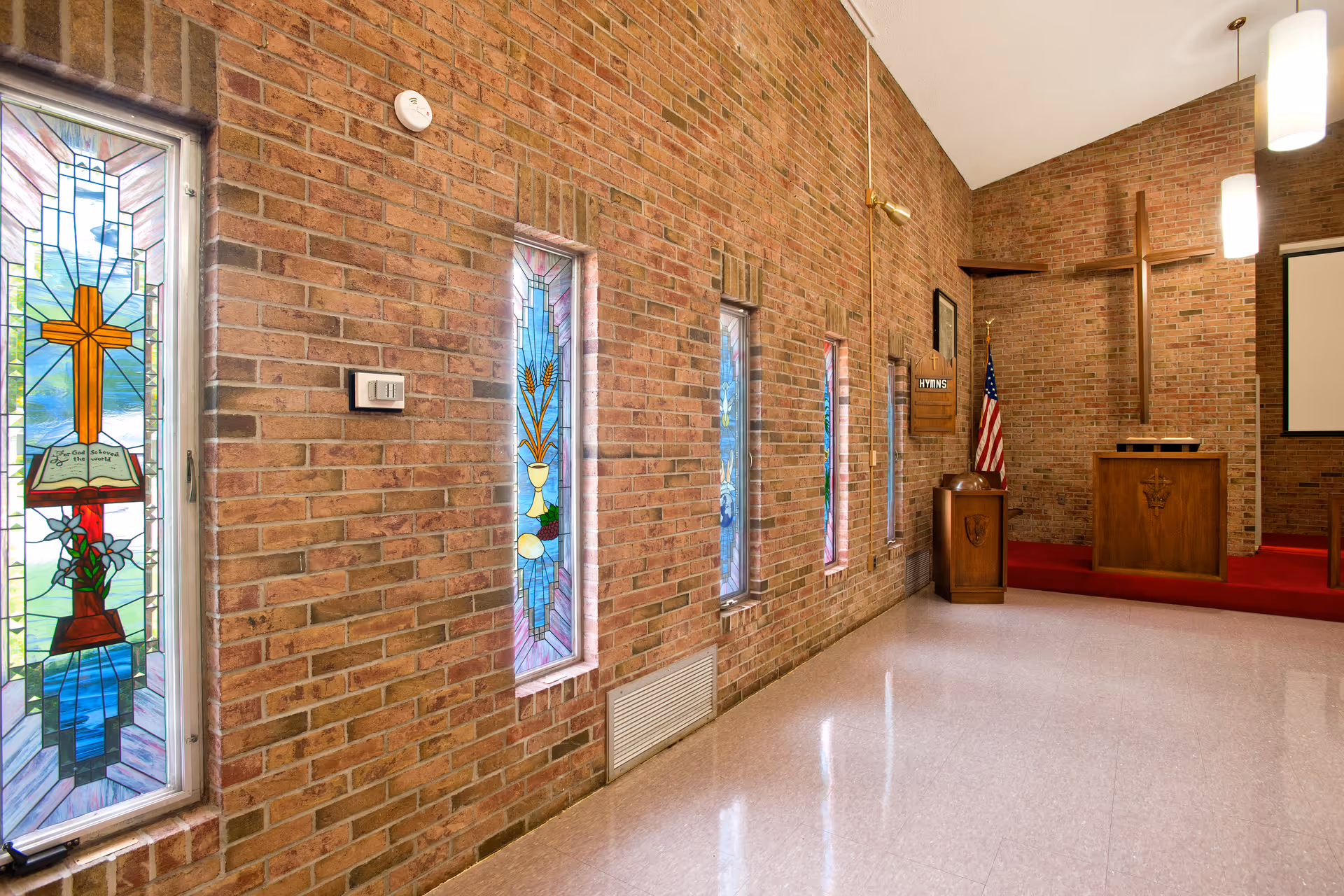 Interior chapel with brick walls, stained glass windows, a wooden pulpit, a large cross and an American flag.