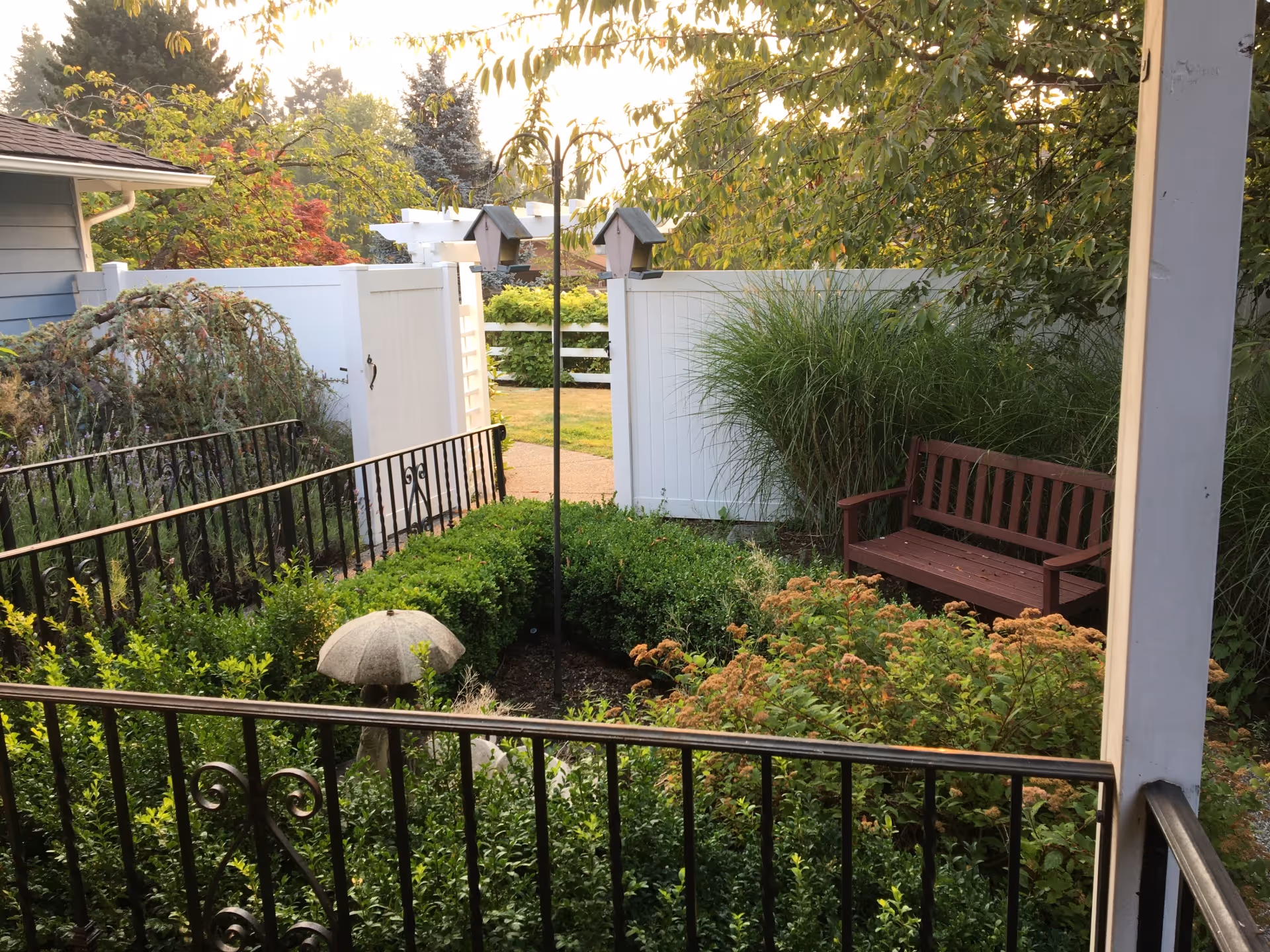 Small enclosed garden with a wooden bench, birdhouses, white fence, and wrought-iron railing.