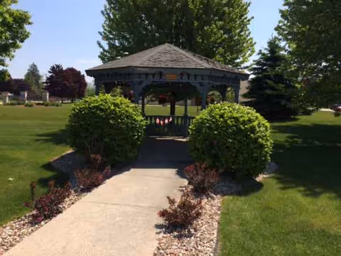 A gazebo sits along a path surrounded by manicured shrubs and green lawn.