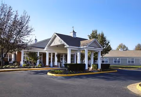 Front view of a white senior living facility with a covered entrance and circular driveway