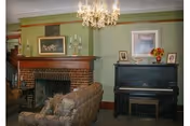 A living room with a brick fireplace, upholstered sofa, chandelier, and an upright piano against a green wall.