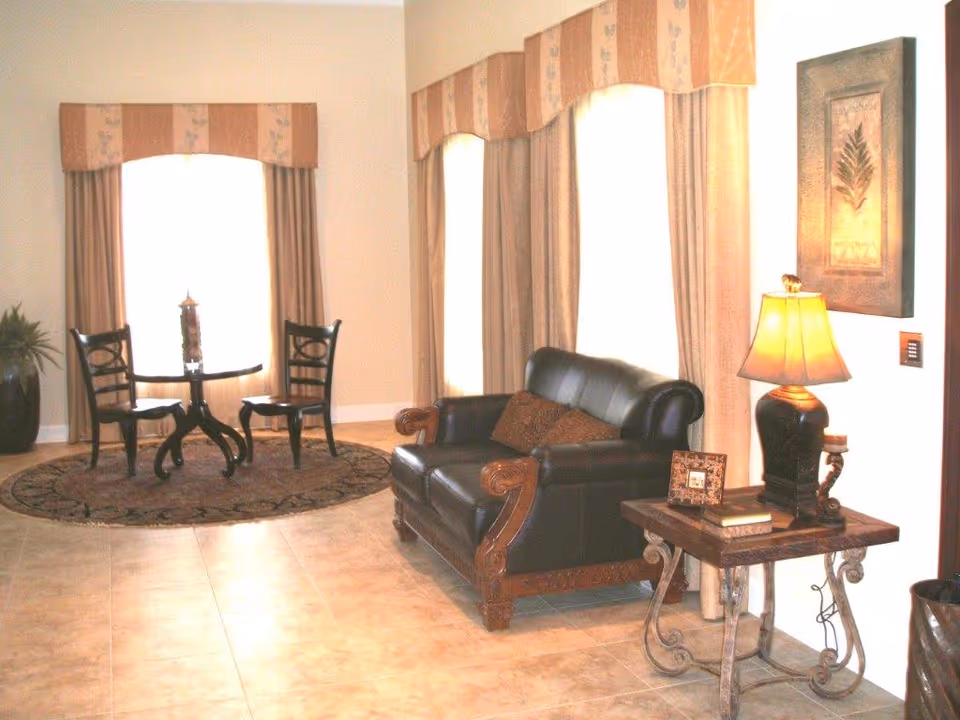 Sunny living-area with a black leather loveseat, round table and chairs by large arched windows, and a side table with a lamp.