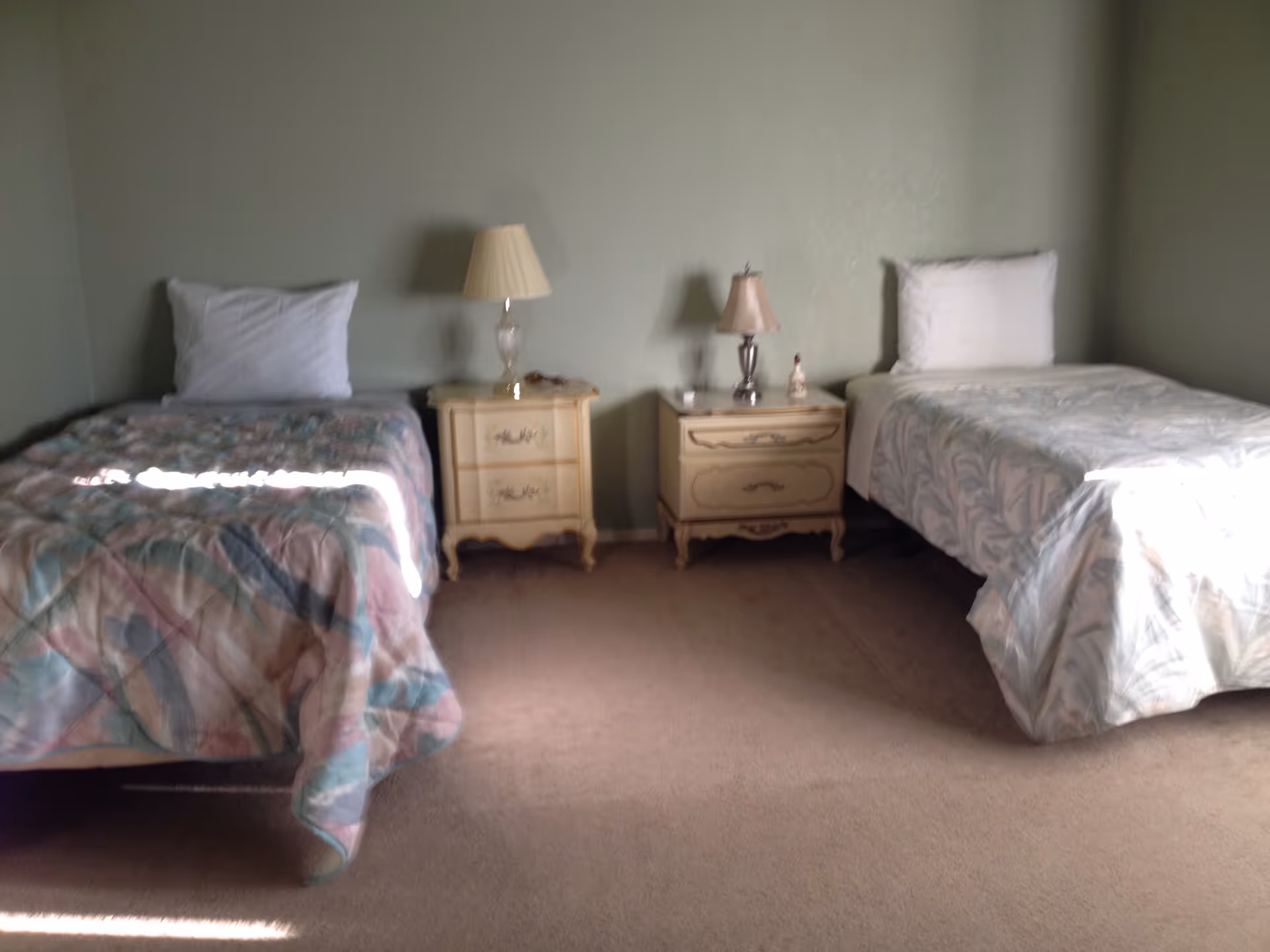 A bedroom with two twin beds separated by nightstands topped with lamps against a pale green wall.