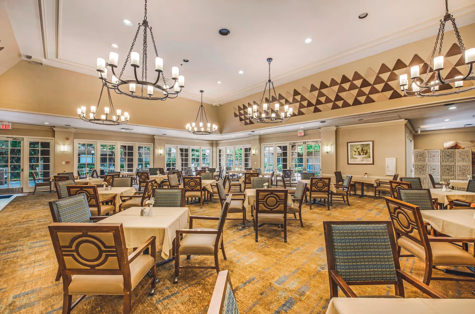 Spacious dining room with multiple tables and chairs, chandeliers, and large windows.