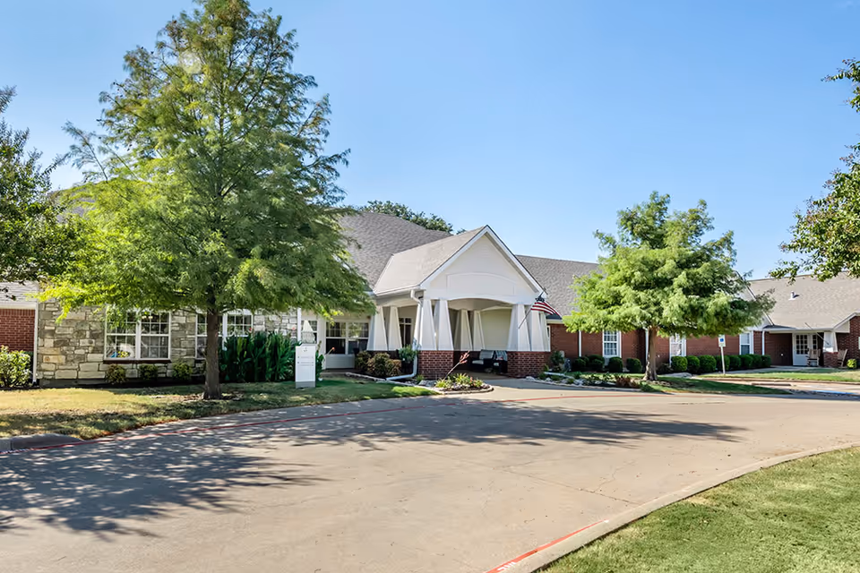 Exterior view of Brookdale Waxahachie entrance with white facade, brick accents, and trees.