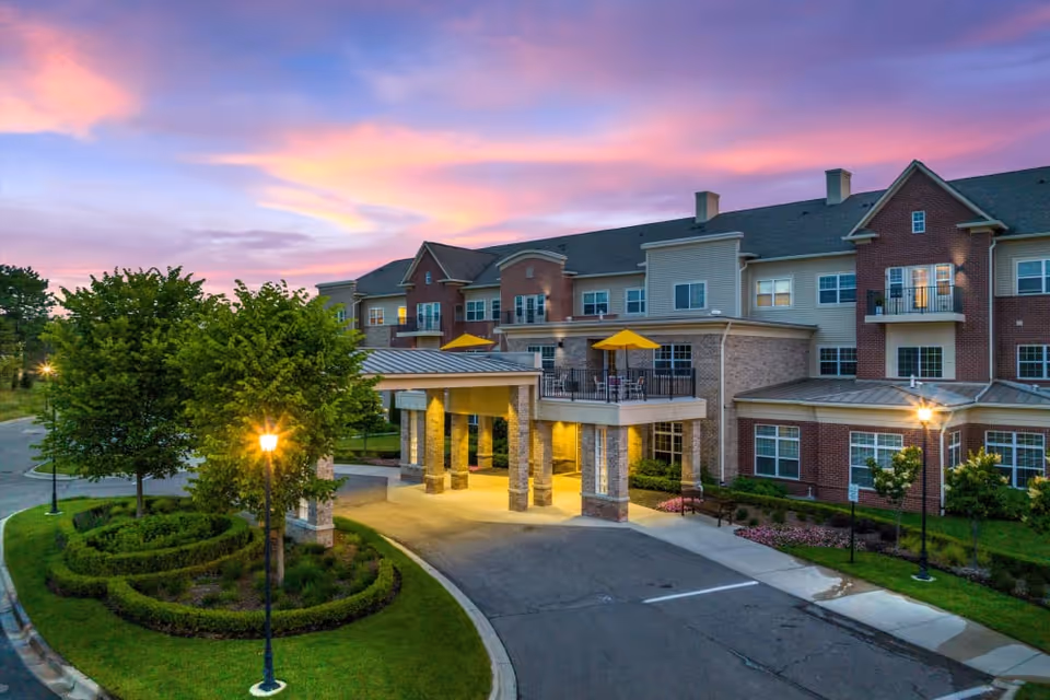 Exterior view of a senior living facility with entrance canopy and sunset sky.