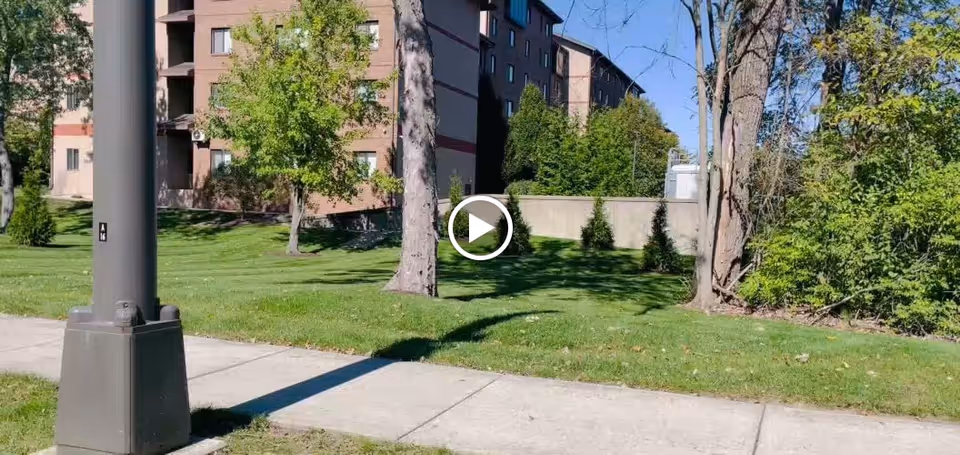 Sidewalk and grassy lawn in front of a multi-story brick building with trees and a lamppost.
