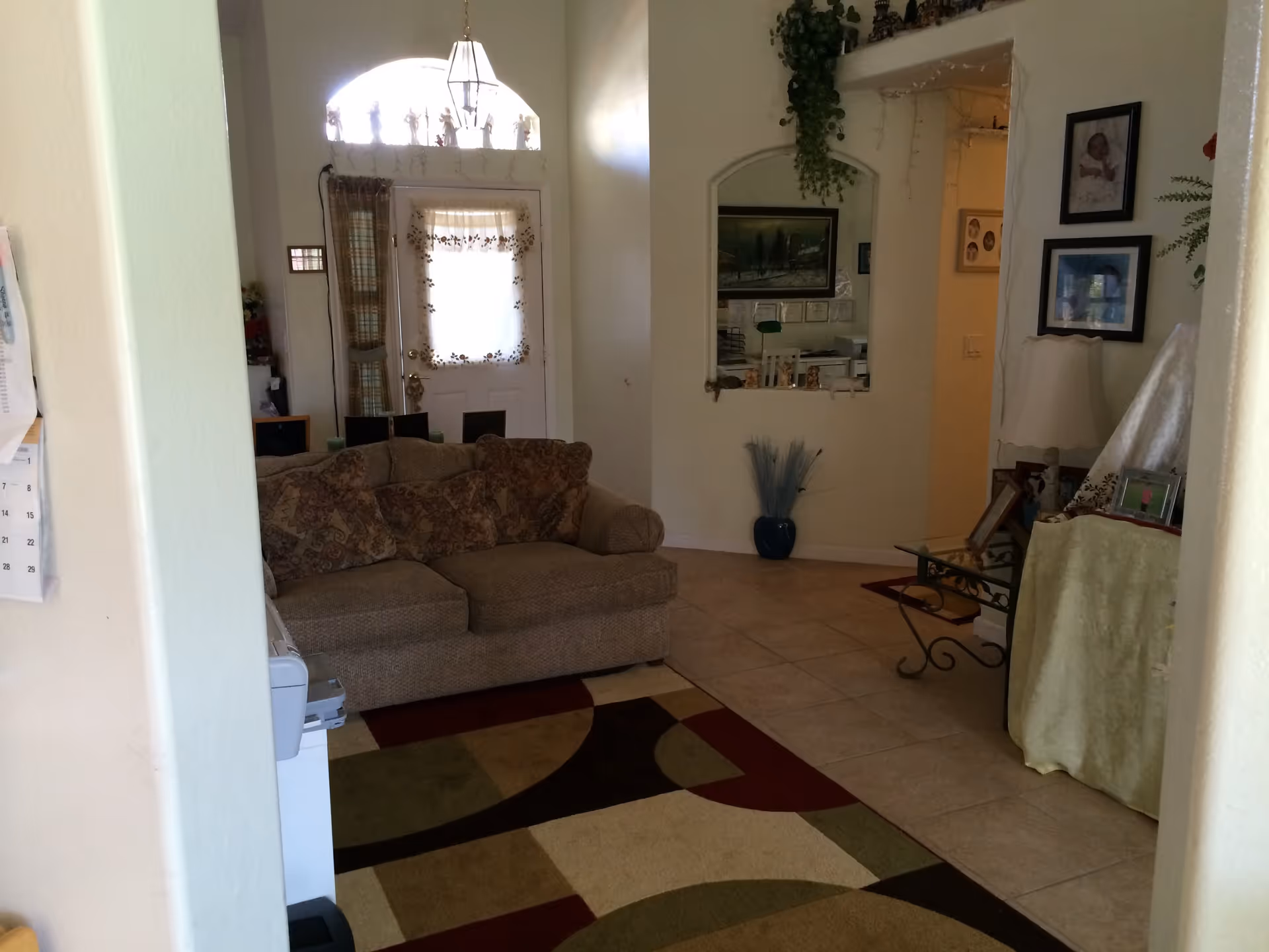 A living room with a beige sofa, patterned area rug, and an entry door with decorative window.