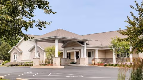 Single-story senior living facility exterior with a covered entrance and parking lot.