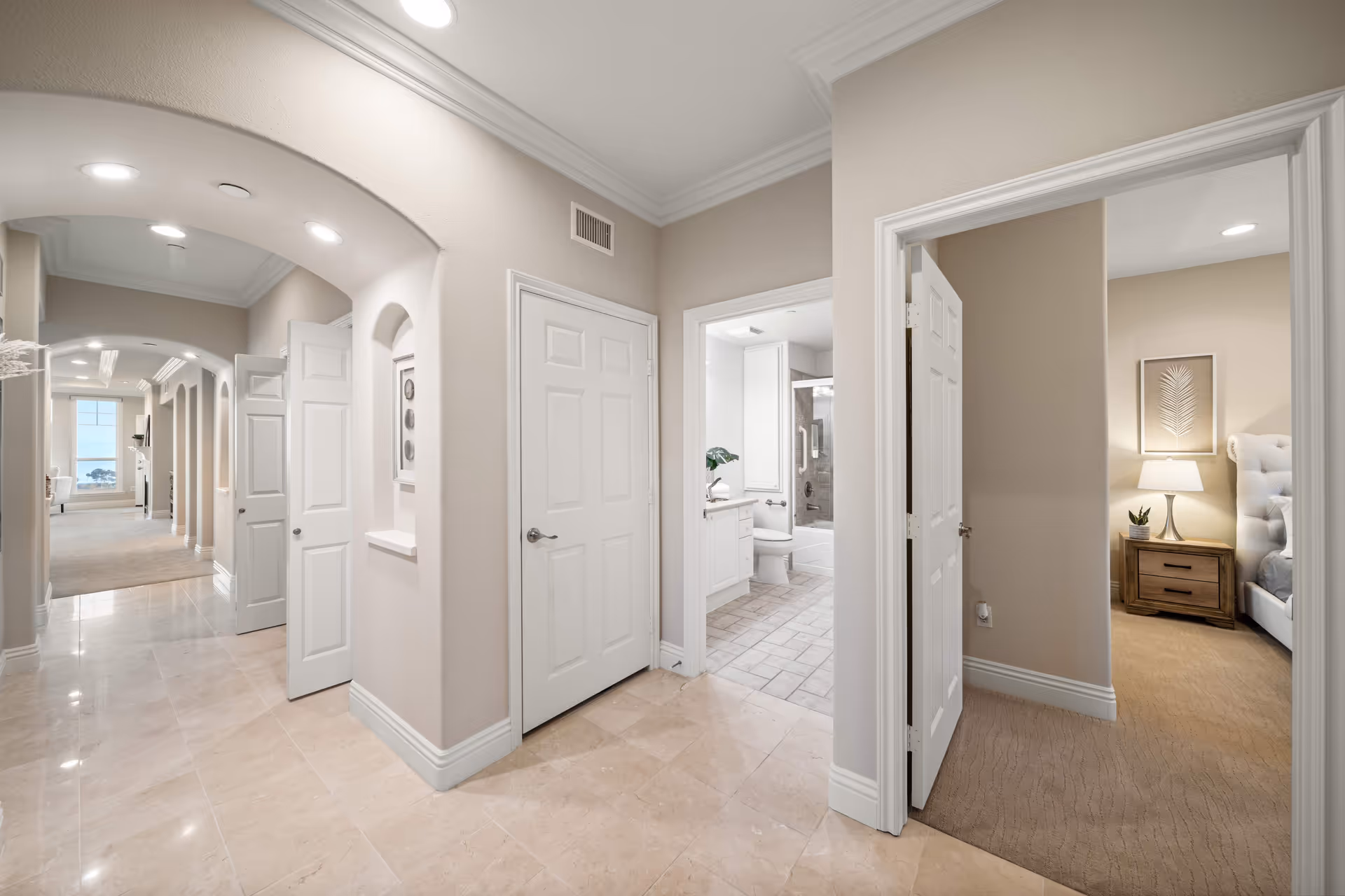 A well-lit hallway in Sea Bluffs, featuring multiple doors leading to rooms, with a view of a bathroom and a bedroom at the end of the corridor.