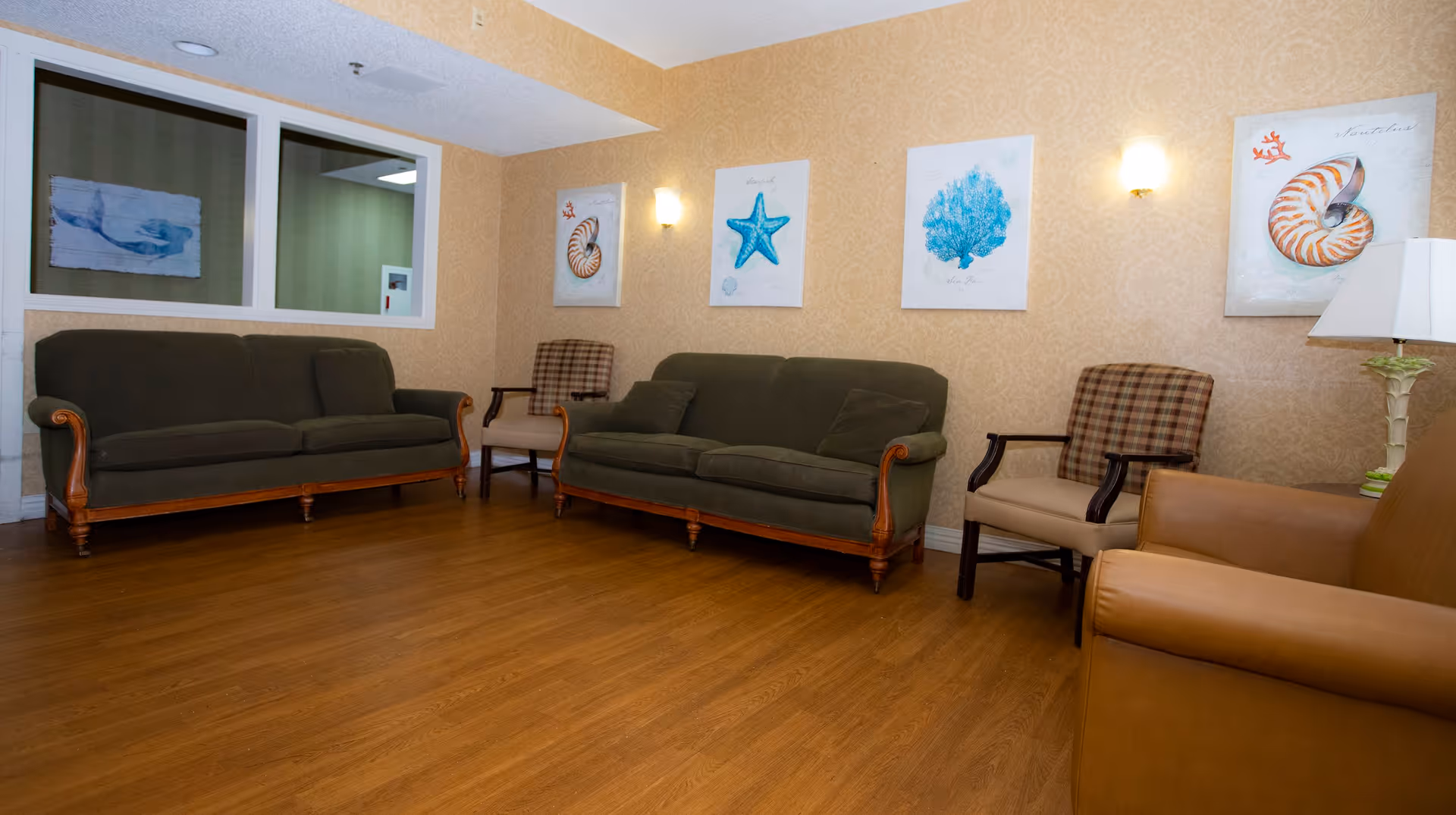 Seating area with sofas and chairs against a wall decorated with sea-themed artwork in a senior living facility.