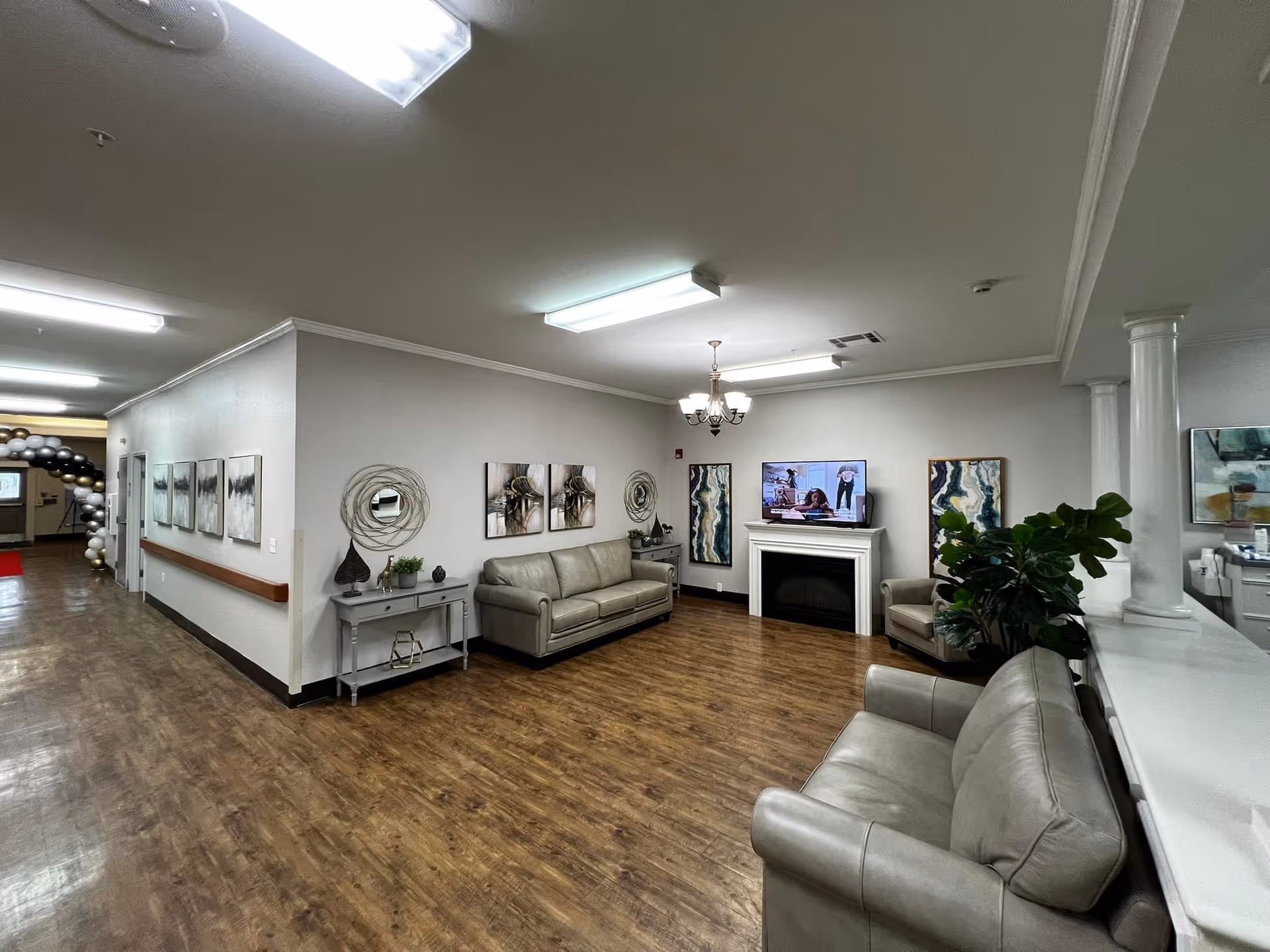 Well-lit common living room area with leather sofas, a TV above a fireplace, wall art, and wood flooring.