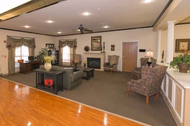 Communal living room with sofas, armchairs, a fireplace, a desk, and decorative plants.