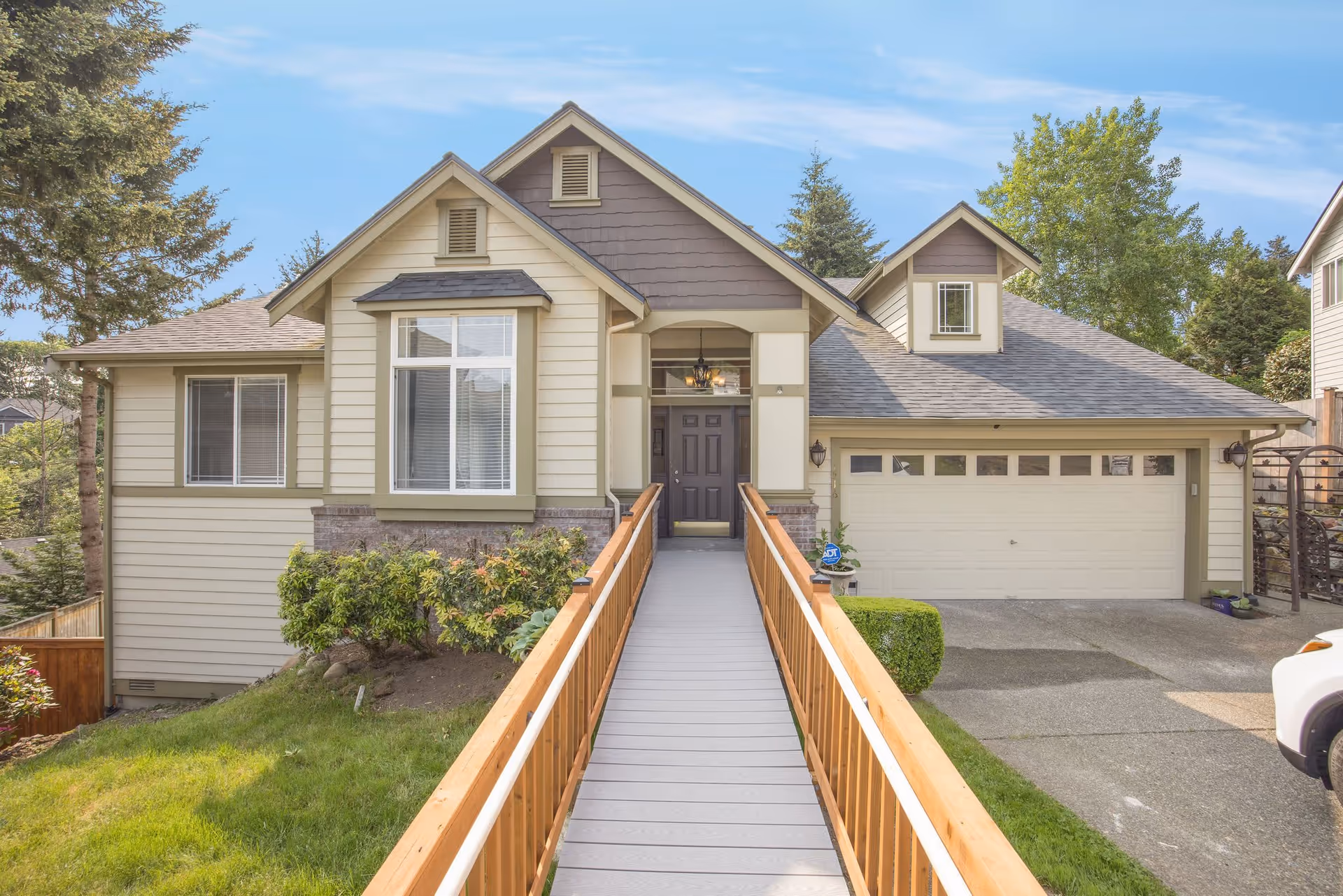 Front exterior of a light-colored suburban house with a long wooden ramp leading to the front door and an attached two-car garage.