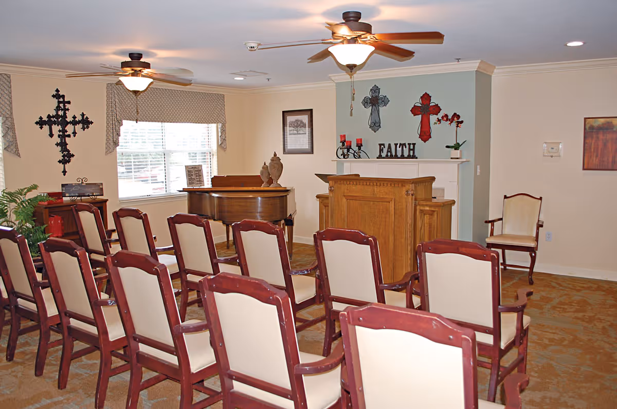 Small chapel-style meeting room with rows of chairs facing a wooden lectern and piano, wall crosses and the word "FAITH" on the wall.