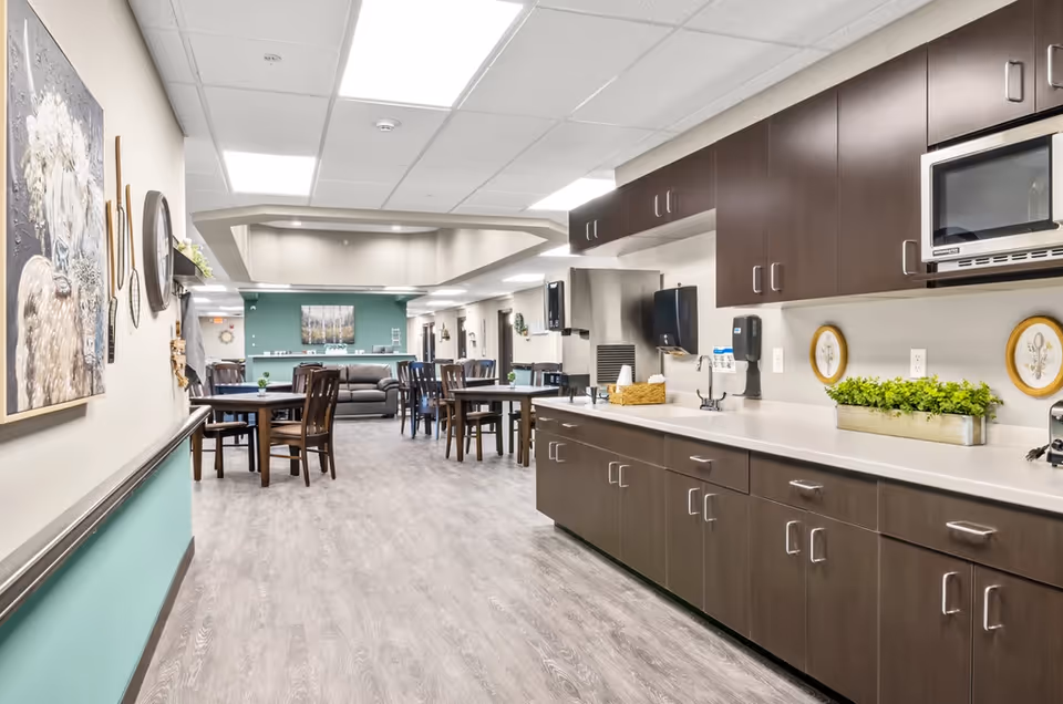 Communal dining and lounge area with tables and chairs and a long kitchenette with dark cabinets along the right wall.