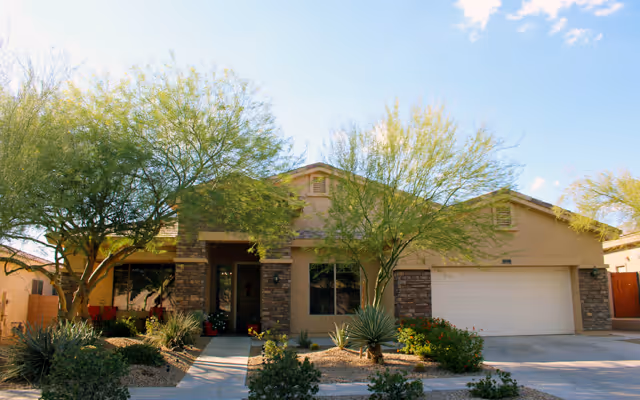 Single-story beige assisted living facility with stone accents, front entrance, and desert landscaping.