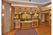 Reception area of a senior living facility with a wooden front desk, pendant lights hanging from the ceiling, decorative wall panels, and a hallway leading to other rooms.