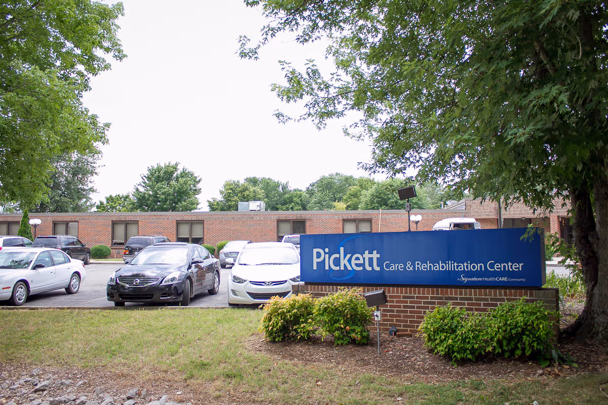 Front sign for Pickett Care & Rehabilitation Center with parked cars and a single-story brick building behind it.