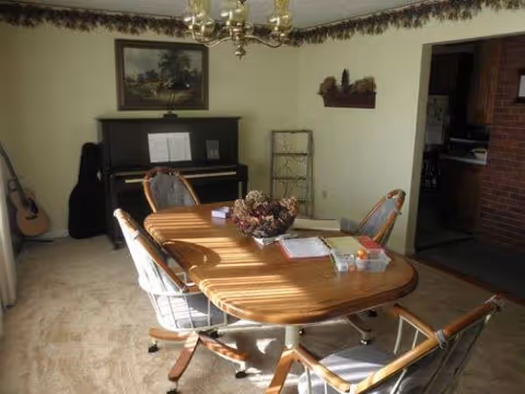 A dining room with a wooden table, chairs, piano, and wall decor.