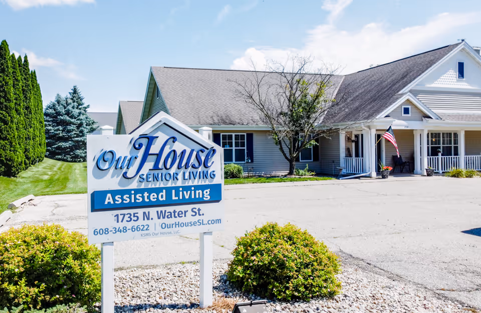 Exterior front of Our House Senior Living assisted living facility with a prominent sign and a one-story building entrance displaying an American flag.