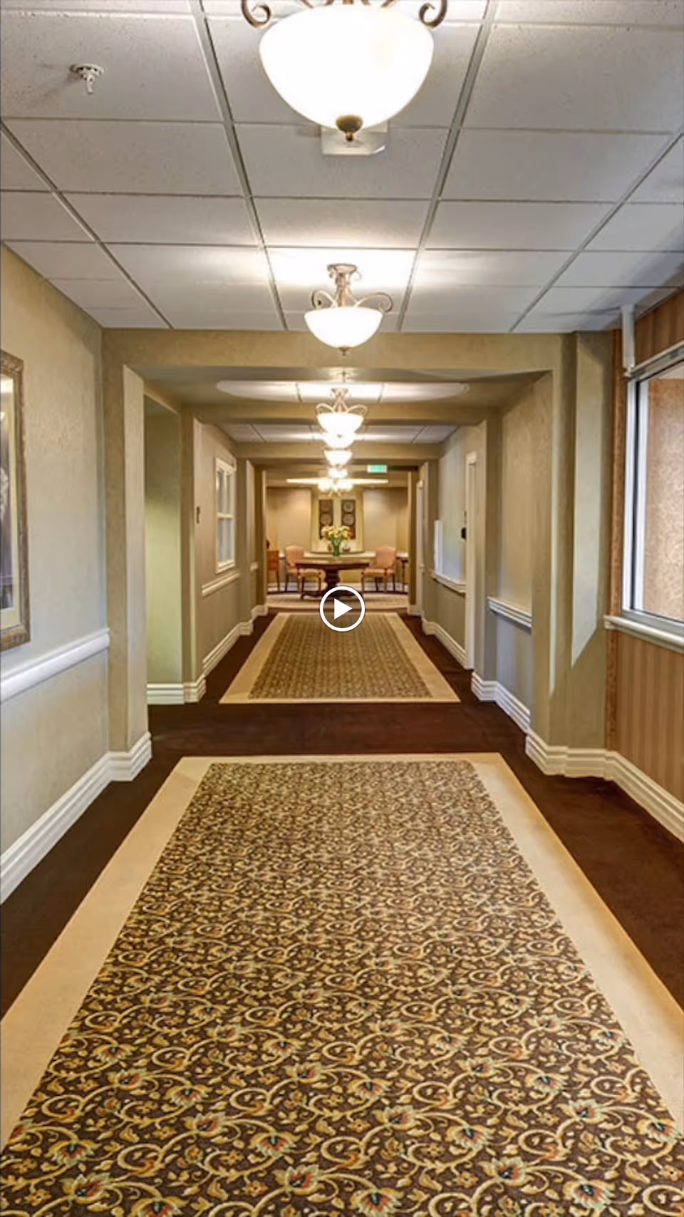 Carpeted interior hallway with patterned runners, ceiling lights, and a seating area visible at the far end.