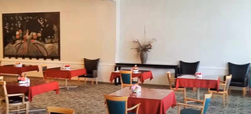 A dining room with several small tables covered in red tablecloths, chairs, wall art, and a floral arrangement.