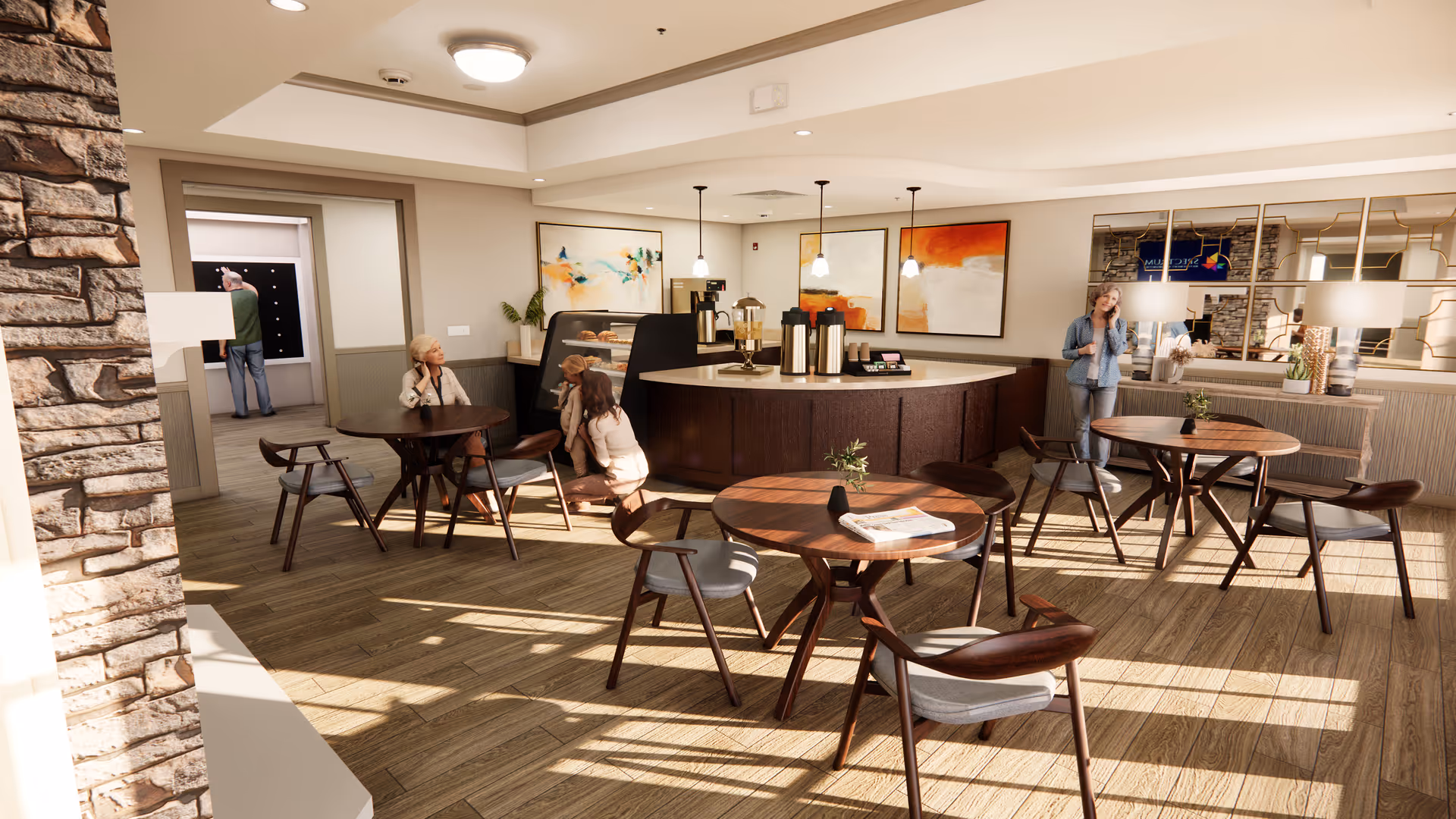 A bright and spacious common area in a senior living facility with wooden round tables and chairs arranged on a wood floor. There is a curved counter with coffee dispensers and a display case, and three pendant lights hanging above it. Several people are present, including two women sitting and talking near the counter, a woman standing and talking on the phone, and a man in the background near a doorway. The walls are decorated with abstract paintings and a large mirror with a decorative frame.