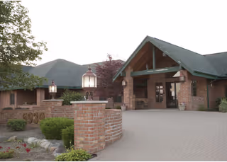 Brick senior living campus entrance with a covered porch, lamps, and landscaping.