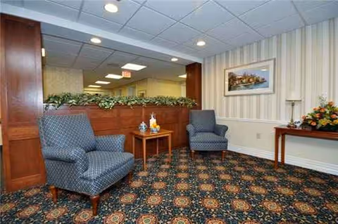 Two blue upholstered armchairs with a small table between them in a patterned carpeted lounge area.