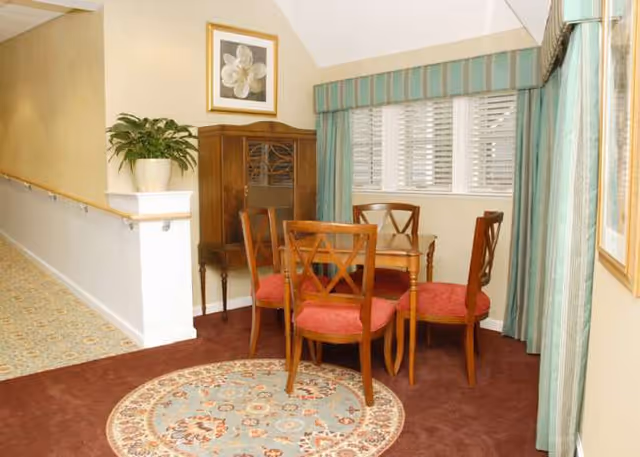 Small dining area in a senior living interior with chairs, rug, cabinet and window.