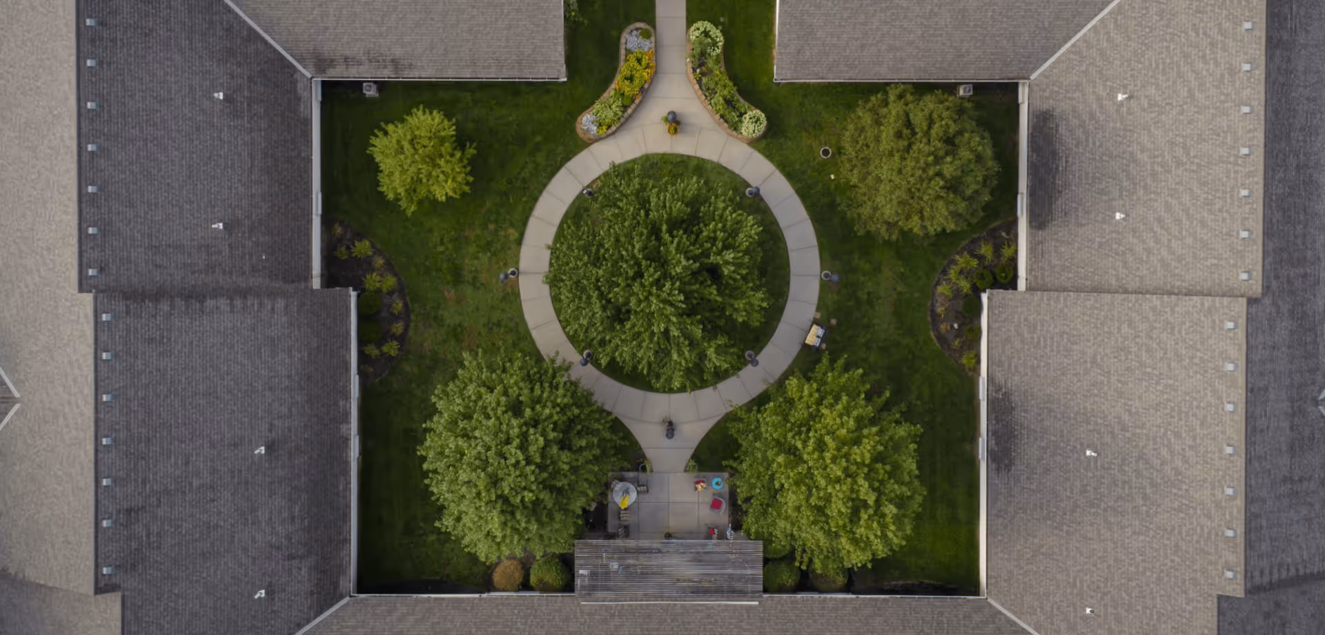 Aerial view of a central circular courtyard with pathways, trees, benches, and surrounding building roofs.