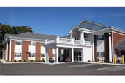 Front exterior of a two-story brick and white-columned health and rehabilitation center with a covered entrance and parking area.