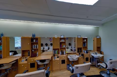 Interior hair salon with multiple styling chairs, mirrors, wash basins, and wooden storage cabinets.