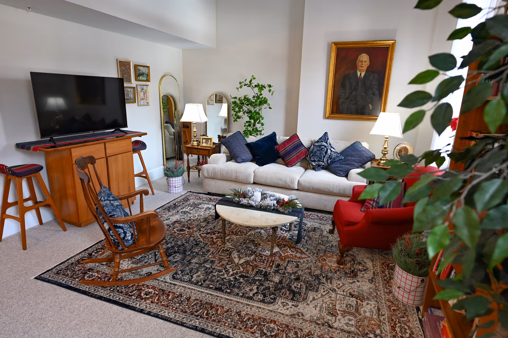 Cozy living room with a white sofa, red armchair, wooden rocking chair, TV on a stand, coffee table and patterned rug.