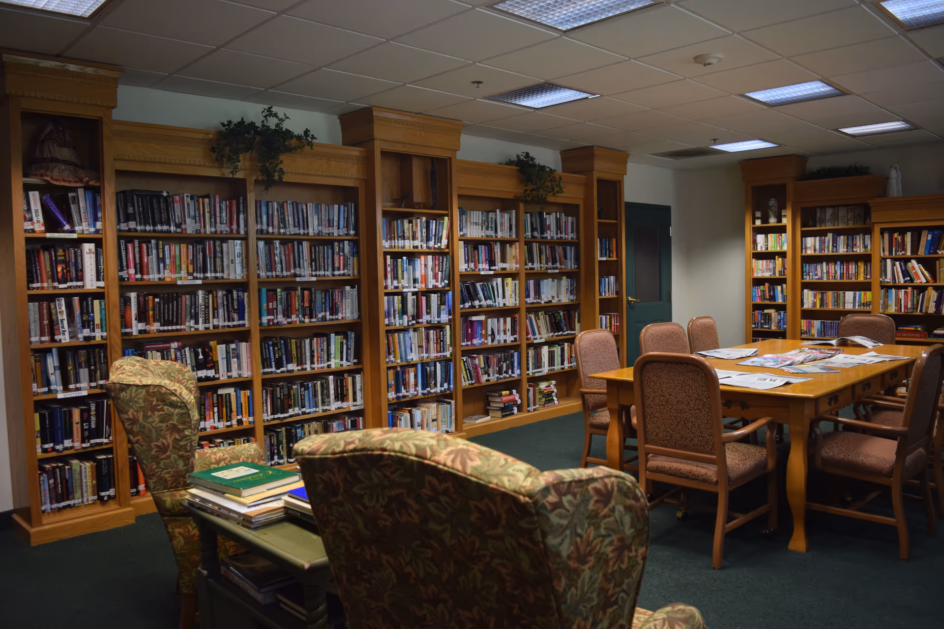 Library-like lounge in a retirement community with tall bookcases, a table, and upholstered chairs.
