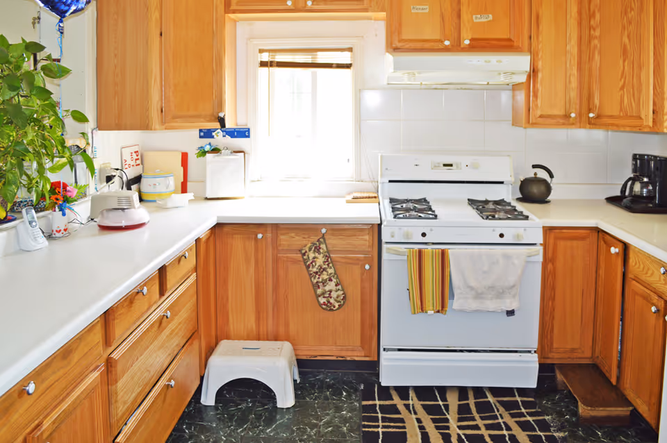 Bright kitchen with oak cabinets, a white gas stove, countertops holding small appliances and a plant, and a step stool on the floor.