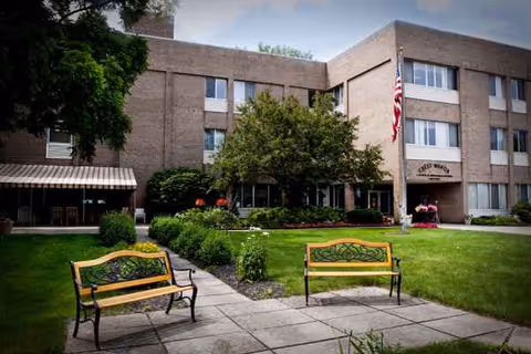 Brick Crest Manor exterior with benches, flag, shrubs, and an entrance.