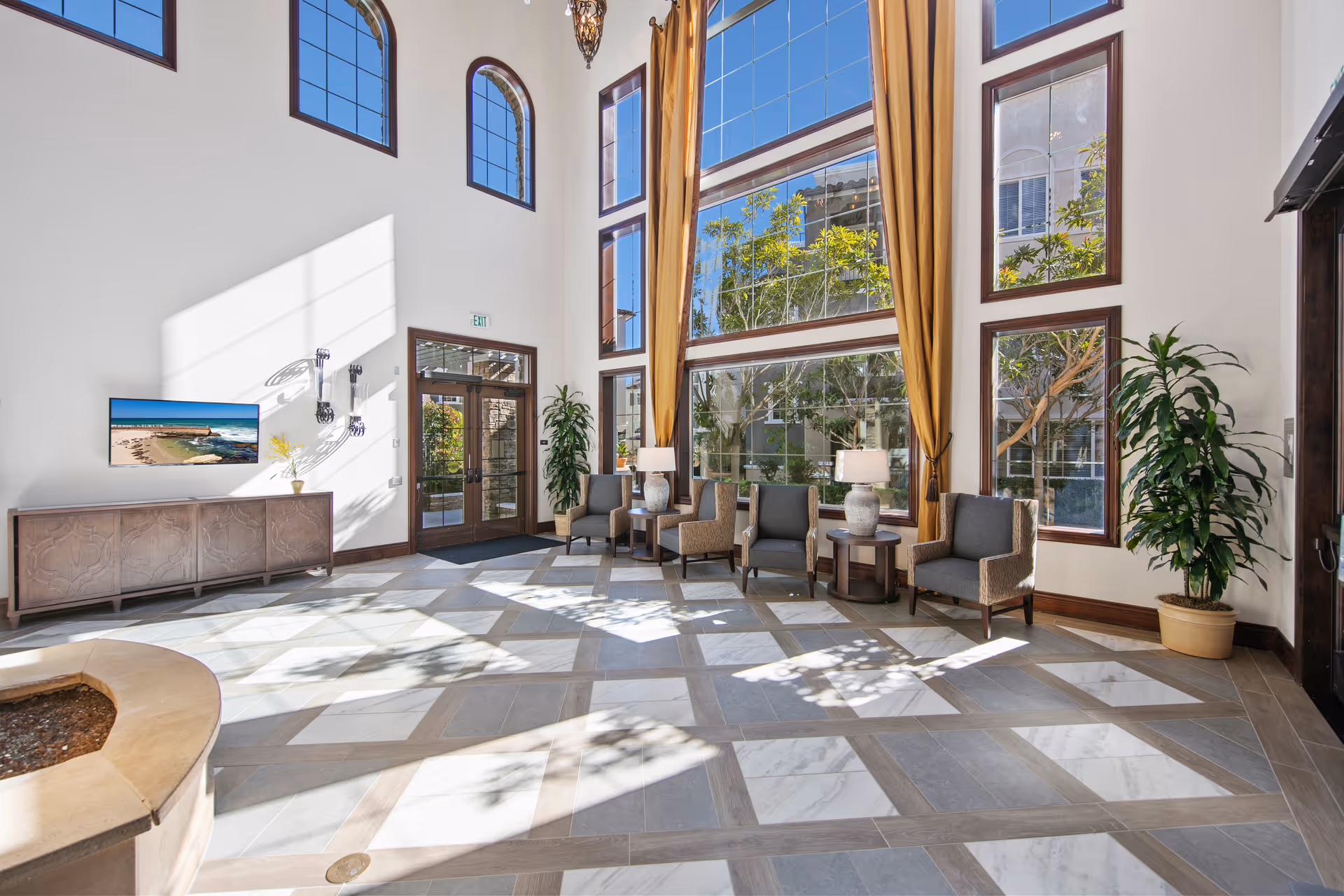 Bright two-story lobby with tall windows, seating area, potted plants, and a patterned tile floor.