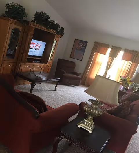 Senior facility living room with leather chairs, coffee table, and TV.