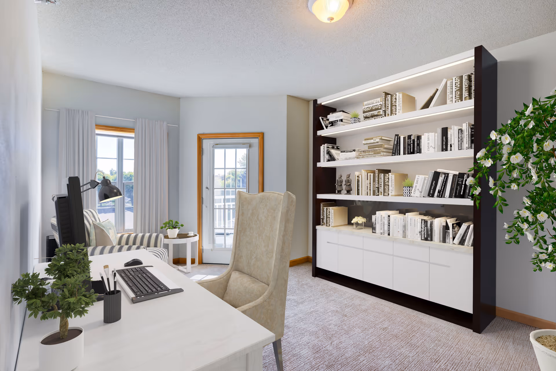 A bright and cozy interior room featuring a white desk with a computer keyboard and mouse, a beige upholstered chair, a striped armchair near a window with white curtains, a small round side table with a plant, a large bookshelf filled with books and decorative items, and a potted plant with white flowers in the corner. A door with glass panes leads to an outdoor area.