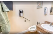 A small bathroom with a toilet, a sink with a granite countertop, a wall-mounted soap dispenser, a hand towel hanging on a rack, and a framed picture on the wall.