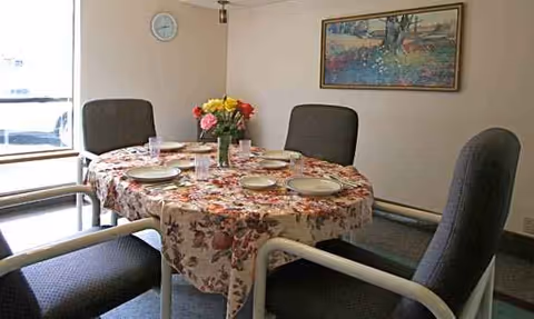Round dining table with floral tablecloth and place settings in a senior living dining room.