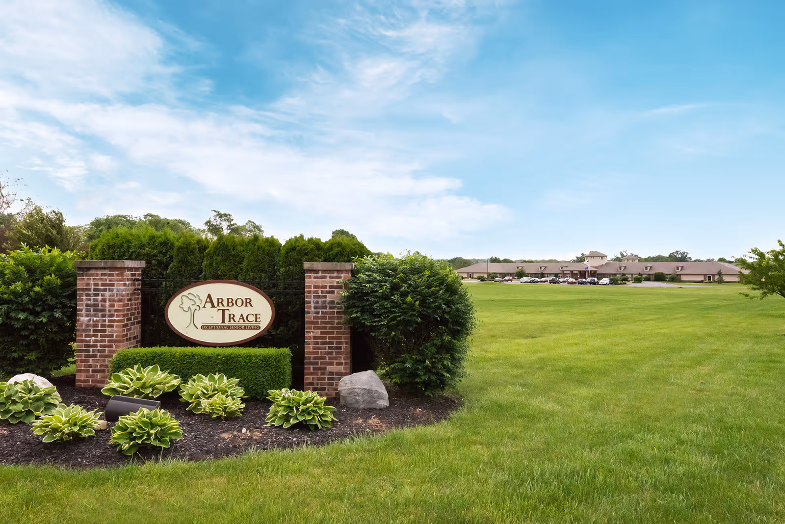 Entrance sign reading 'Arbor Trace' on a landscaped lawn with the senior living building visible in the background.